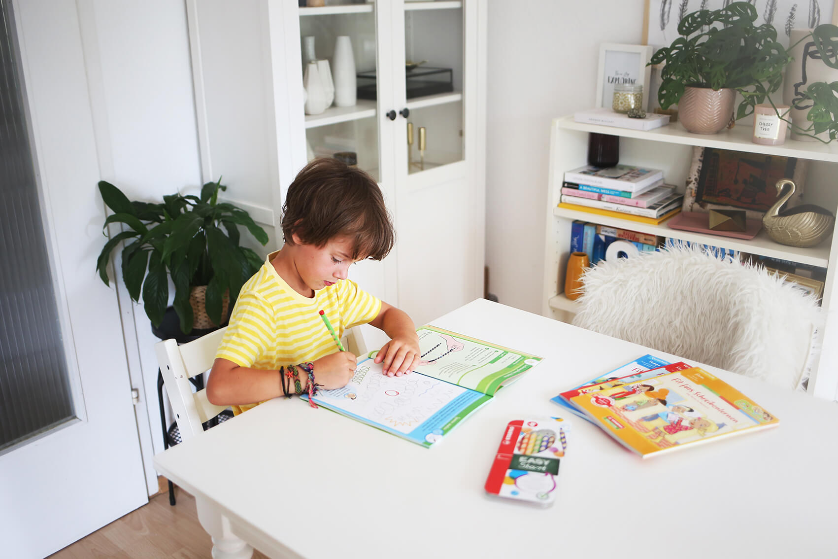 Test Kind in gestreiftem Shirt, das an einem hellen Tisch in einem Übungsheft zeichnet.