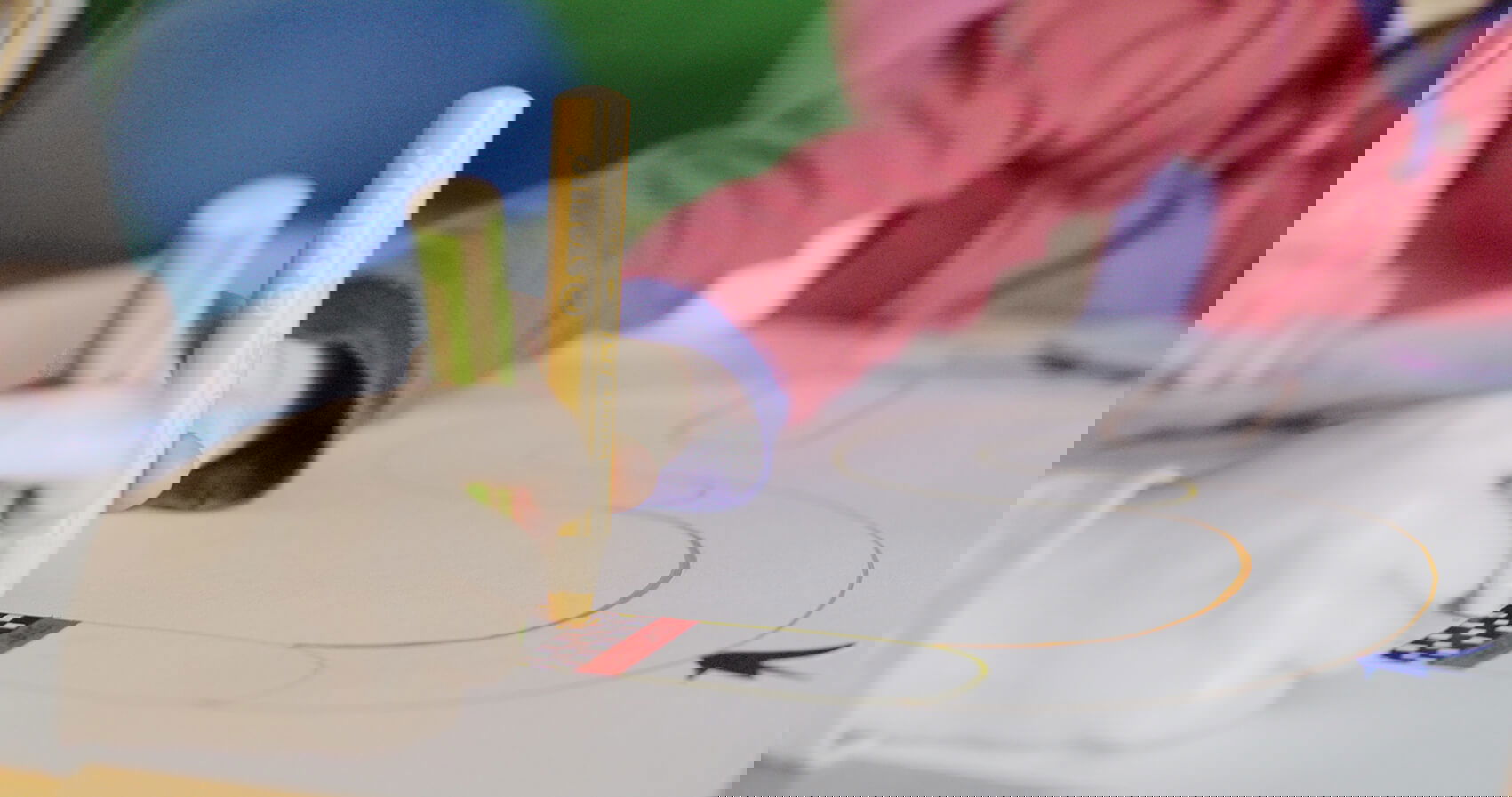 Kinder zeichnen mit bunten Stiften auf Papier, darunter eine Rennbahn.